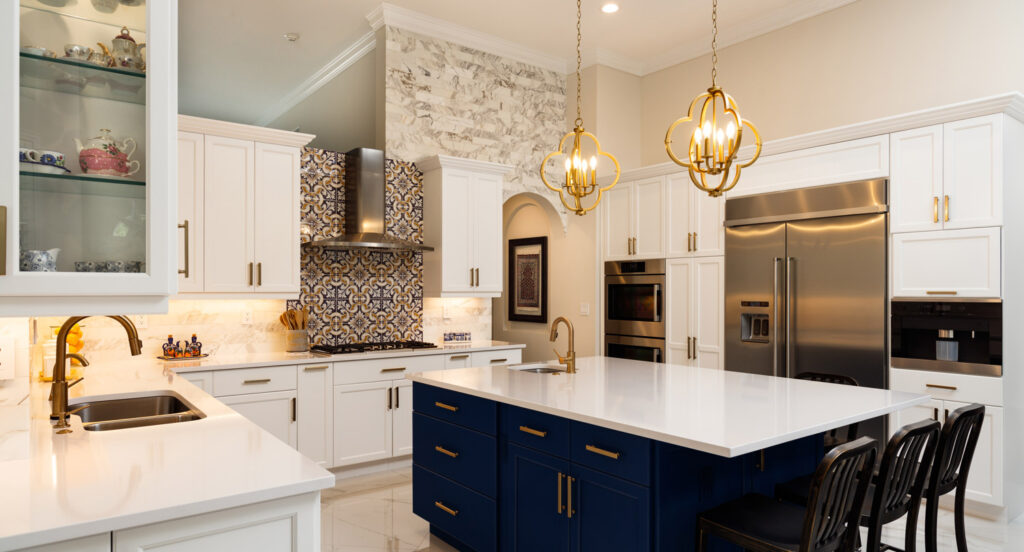 Modern kitchen with white cabinets, blue island, gold fixtures, stainless steel appliances, patterned backsplash, and two pendant lights over the island.